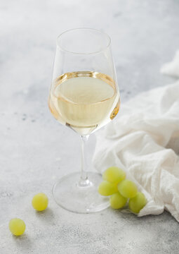 Glass of white wine with grapes and linen cloth on light background.