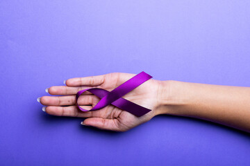 Cropped hand of african american mid adult woman with purple awareness ribbon on blue background