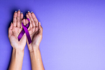 African american mid adult woman's hands with purple awareness ribbon on blue background, copy space