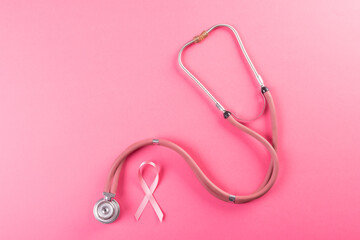Directly above shot of pink breast cancer awareness ribbon and stethoscope on pink background