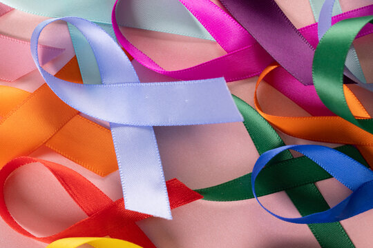 Extreme close-up of various multicolored awareness ribbons on pink background, copy space