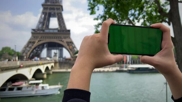 Phone with green Chromate screen on the background of the eiffel tower. in Paris using her cell phone in front of Eiffel Tower, seine bridge background, . High quality 4k footage