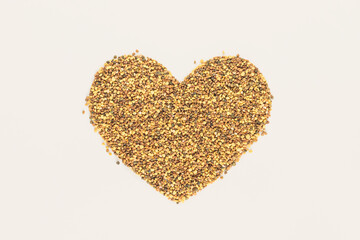 A heart-shaped pile of golden-yellow bees pollen on a isolated pastel beige background. Nature...