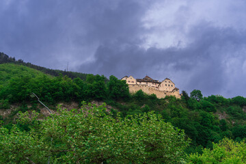 Fototapeta na wymiar Lonely castle in the forest on a mountain above the city of Vaduz in the Principality of Liechtenstein on an overcast spring evening against a dramatic cloudy sky, Europe travel backdrop