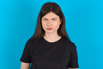 young caucasian woman wearing black T-shirt over blue background frowning his eyebrows being displeased with something.