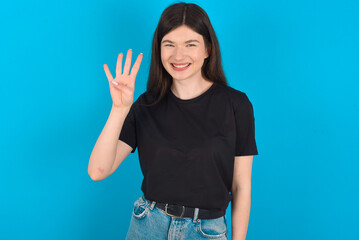 Fototapeta na wymiar young caucasian woman wearing black T-shirt over blue background showing and pointing up with fingers number four while smiling confident and happy.