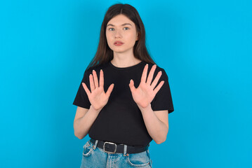 young caucasian woman wearing black T-shirt over blue background doing stop sing with palm of the hand. Warning expression with negative and serious gesture on the face.
