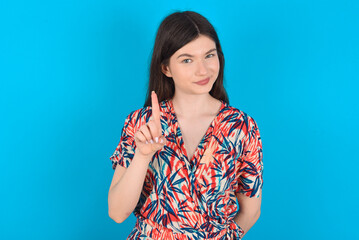 No sign gesture. Closeup portrait unhappy young caucasian woman wearing floral dress over blue background raising fore finger up saying no. Negative emotions facial expressions, feelings.