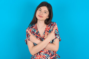 young caucasian woman wearing floral dress over blue background crosses arms and points at different sides hesitates between two items or variants. Needs help with decision