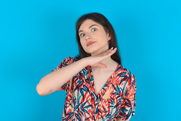young caucasian woman wearing floral dress over blue background cutting throat with hand as knife,...