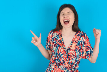 Cheerful young caucasian woman wearing floral dress over blue background showing copy space ad celebrating luck
