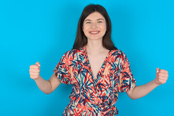 Happy young caucasian woman wearing floral dress over blue background Holding Empty Paper Board Advertising Offer Text Standing. Autumn Advertisement Banner.