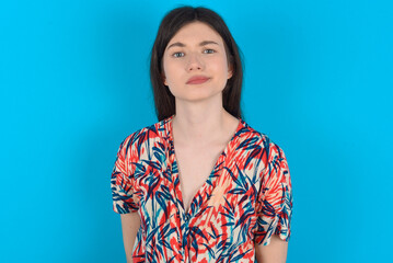 Displeased young caucasian woman wearing floral dress over blue background frowns face feels unhappy has some problems. Negative emotions and feelings concept