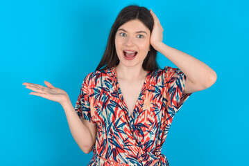 Fototapeta na wymiar Shocked amazed surprised young caucasian woman wearing floral dress over blue background hold hand offering proposition