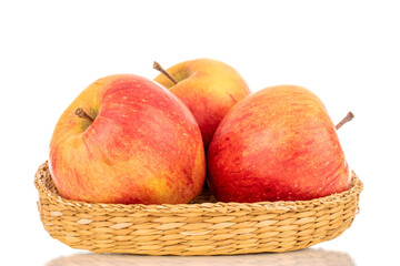 Three juicy organic apples in a straw bowl, close-up, isolated on a white background.