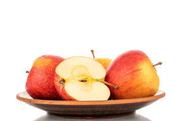 One half and two whole juicy organic apples on a clay dish, close-up, isolated on a white background.