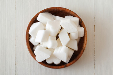 Bridge-shaped beet sugar in wooden bowl on a white wooden table. Flat lay, top down view, no people.