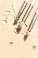 Selective focus makeup brushes on brown background. Spilled water on the table with shiny varied sizes and shapes water drops. Copy space.
