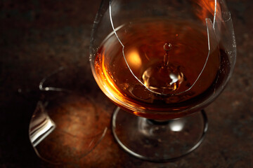 The drop of brandy falls into a broken glass.