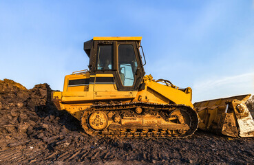 Track bulldozer, earth-moving equipment parking at construction site with bright blue sky background. Land clearing and grading machine for foundation of new building business. Machinery on the ground