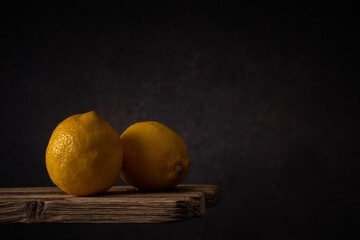 two ripe lemons lie side by side on old boards against a dark backdrop. moody artistic still life with copy space