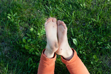 Child's feet are soiled after walking barefoot. Happy childhood. Kid lies on green grass on his...