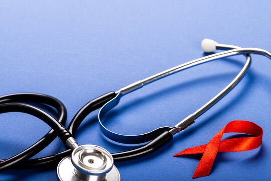 Close-up of stethoscope with red aids awareness ribbon against blue background, copy space