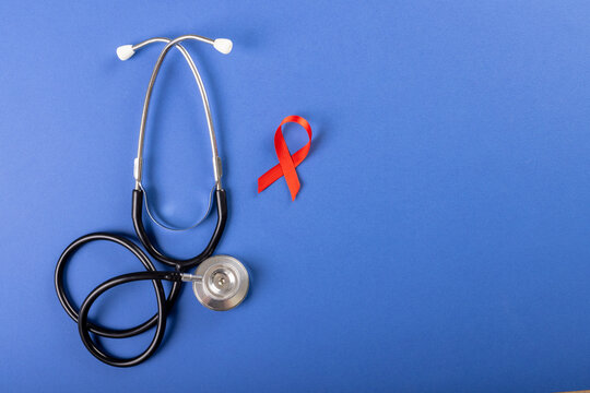 Directly above shot of stethoscope with red aids awareness ribbon over blue background, copy space