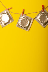 Close-up of condom packages hanging with clothespins on clothesline against yellow background