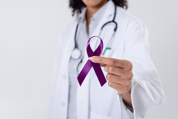 Midsection of african american mid adult female doctor holding purple cancer awareness ribbon