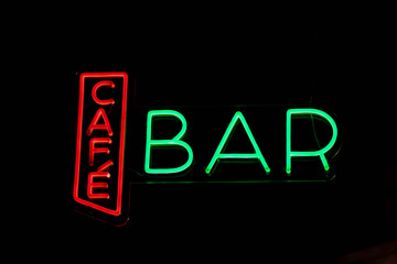 Bright glowing sign with Cafe and Bar colorful words on wall of public pub on black background in city at night time