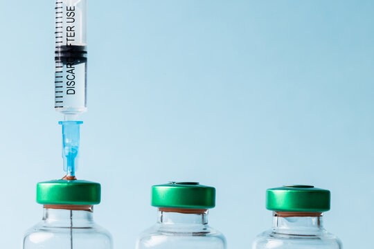 Close-up of syringe with vials arranged against blue background, copy space