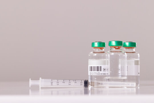 Close-up of syringe with vials on table against white background, copy space