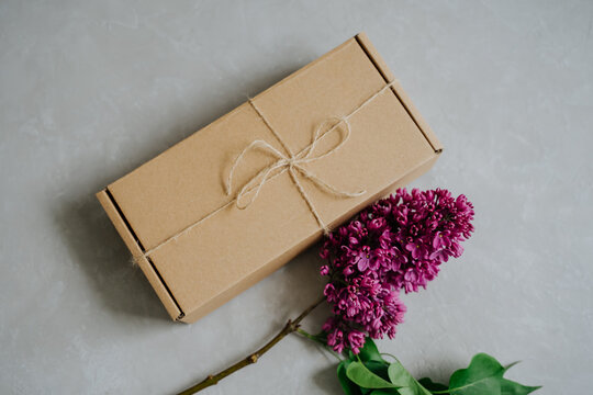 Cardboard box tied with a jute cord. A small package. A branch of lilac. Gift box and flowers.