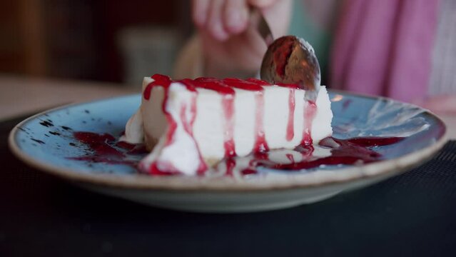 The girl breaks off a piece of strawberry cheesecake with a spoon, lying on a blue plate. Close-up view.