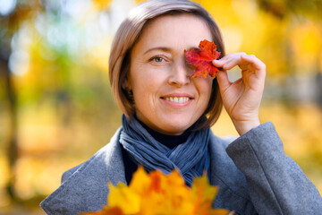 portrait of a beautiful woman with colorful yellow leaves, posing in a city park, bright sunny day in autumn