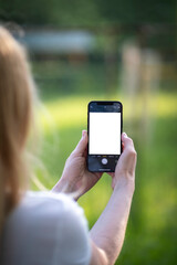 Elderly woman holding a phone with blank screen and photographing nature 
