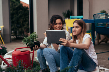 mother and daughter using digital tablet in backyard while gardening