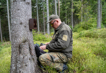 Hunter sets a trail camera on a tree in the forest. Trail cameras are often used by hunters for automatic photography or video shooting of wildlife in the forest.
