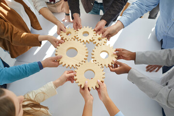 Hands close-up of group multiethnic business people connect wooden gears in the center. Arial view....