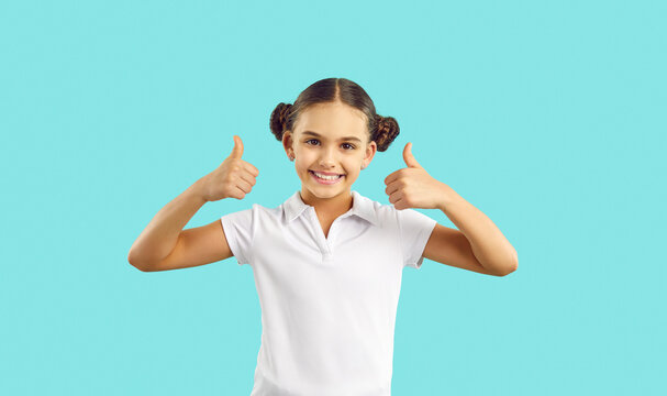 Happy Kid. Joyful Child In Cotton Tennis Tee Says Well Done, Yes, Okay, Excellent, Perfect. Girl In Polo Tshirt, With Cute Hair Buns Standing Isolated On Blue Looks At Camera, Smiles, Gives Thumbs Up