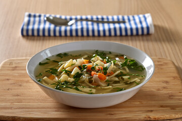 Warm vegetable soup with noodles and fresh chopped herbs on wood
