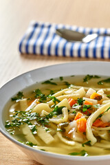 Warm vegetable soup with noodles and fresh chopped parsley on wood