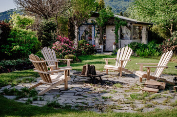 Miejsce na ognisko z fotelami ogrodowymi i altanką ogrodową w tle. Wiosenny ogród z miejscem na ognisku