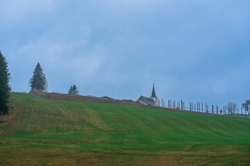 Lonely church on top of a green mountainside in an early rainy morning with rare trees in Austria,...