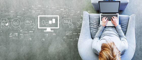 Stock trading theme with man using a laptop in a modern gray chair