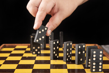 Dominoes, old domino pieces lined up on a board and a hand picking up a piece, dark background,...
