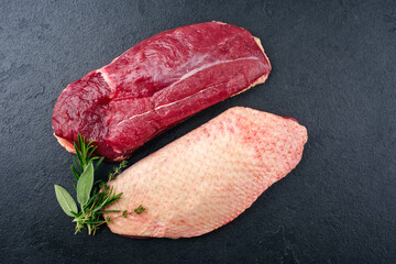 Traditional raw gourmet duck breast filet with skin offered with herbs as top view on a black board