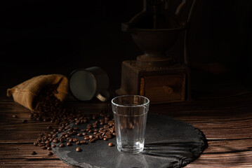 Coffee, empty glass cup and coffee beans on a gray stone over wood, dark food style photo, selective focus.