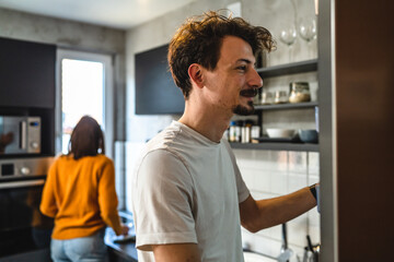 Fototapeta premium Young couple in the kitchen back view husband and wife or boyfriend and girlfriend in the morning daily routine man picking food from the fridge copy space real people